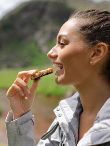 Teen eats granola bar with mountain behind her. How to teach teens and kids positive nutrition habits