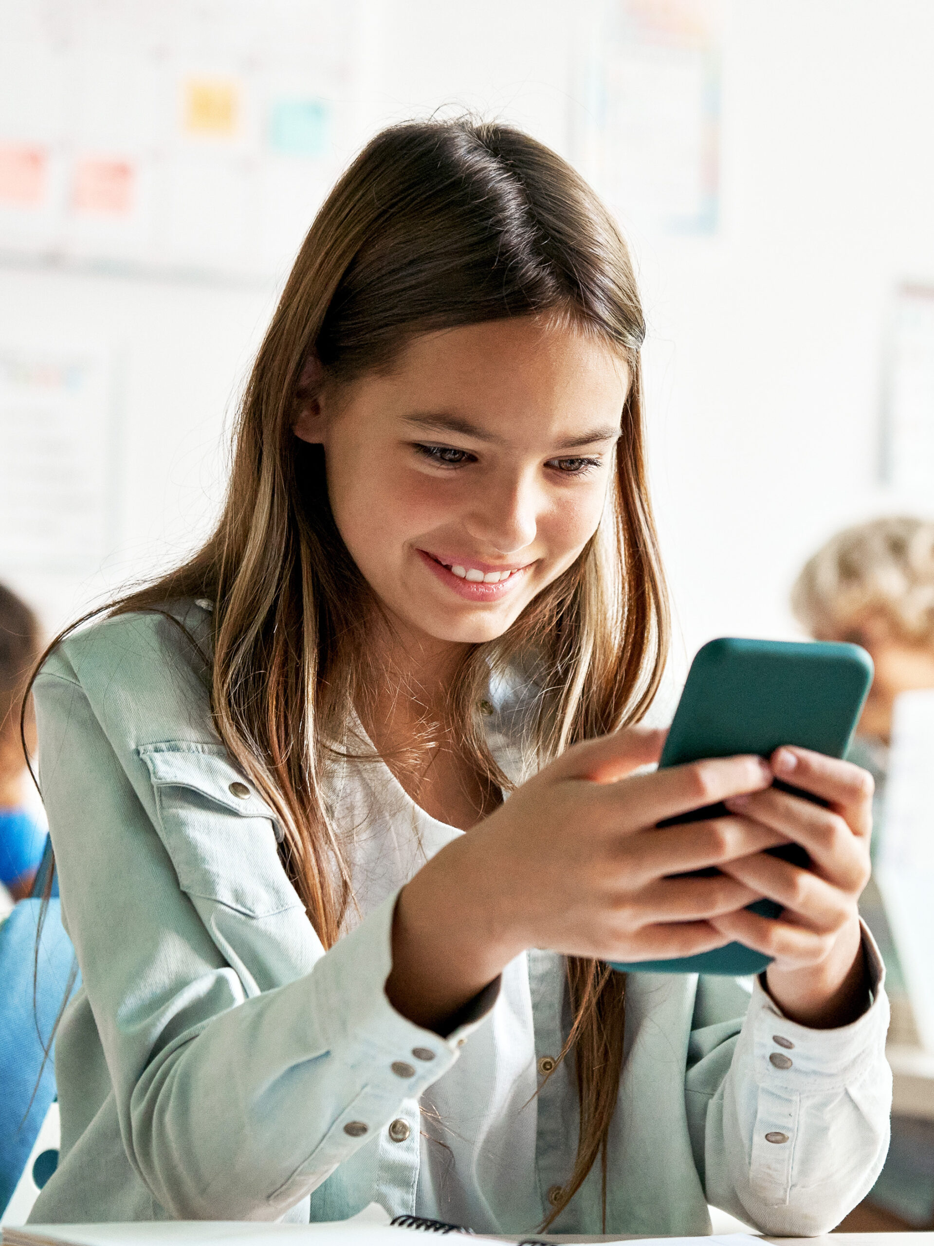 Preteen looks at phone while in class and smiles