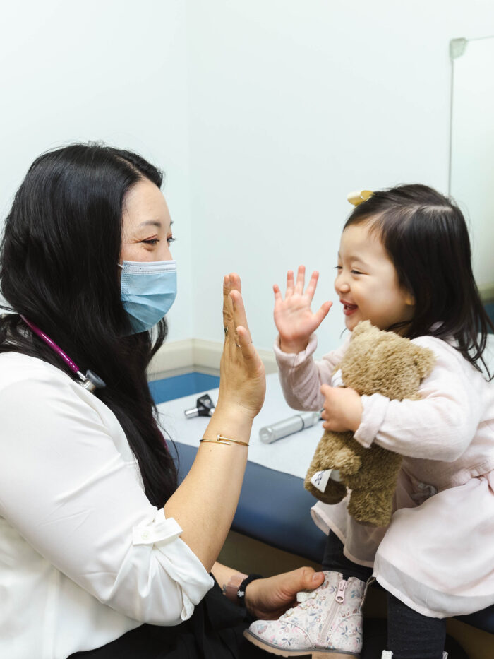 Pediatrician and little girl holding teddy bear high five 