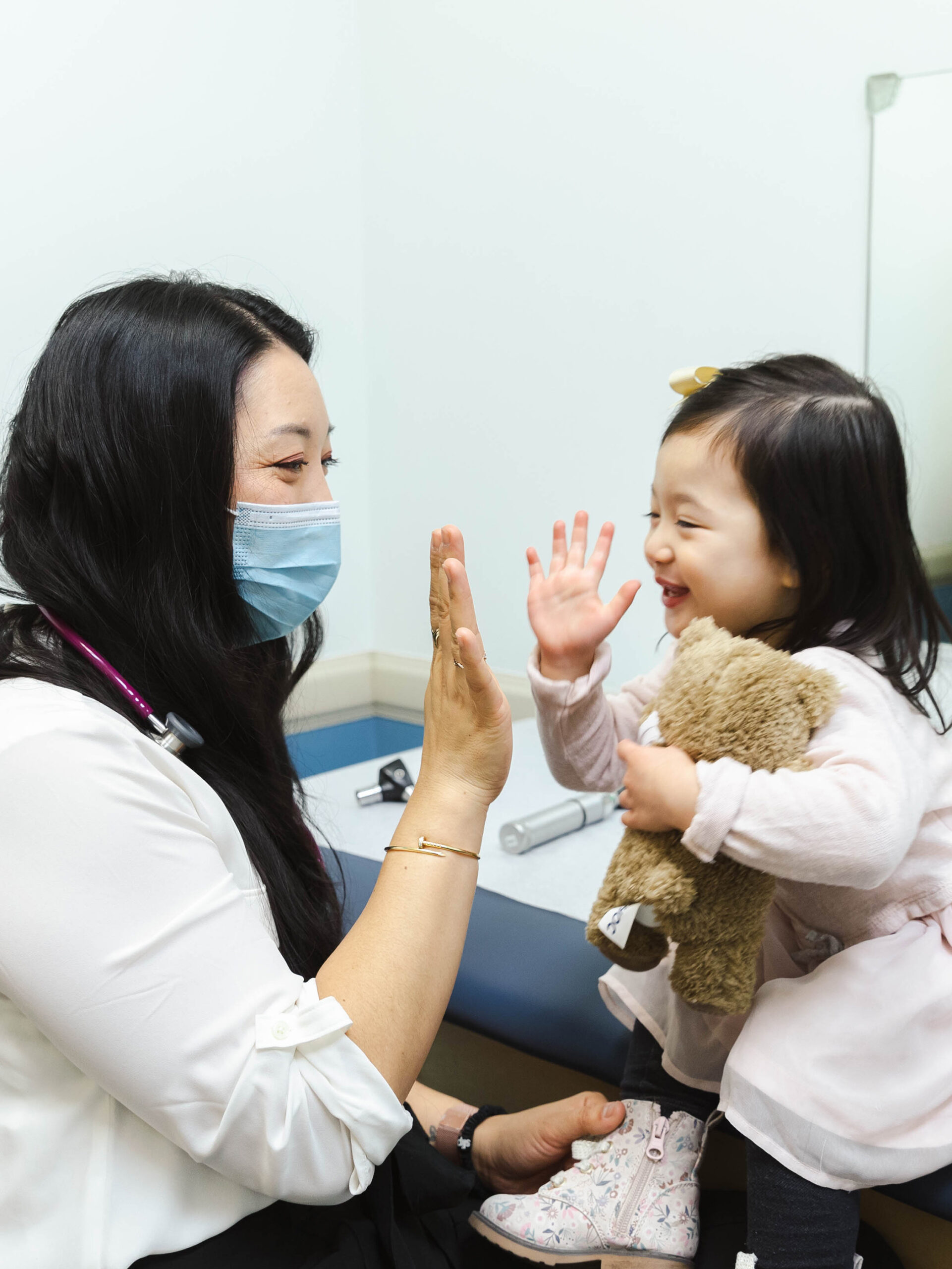 Pediatrician and little girl holding teddy bear high five