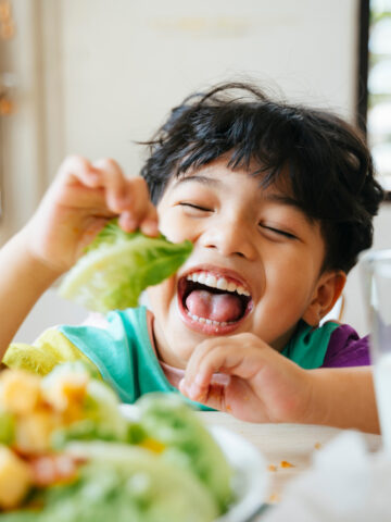 Child smiles while holding lettuce - brain-boosting foods from CHOC