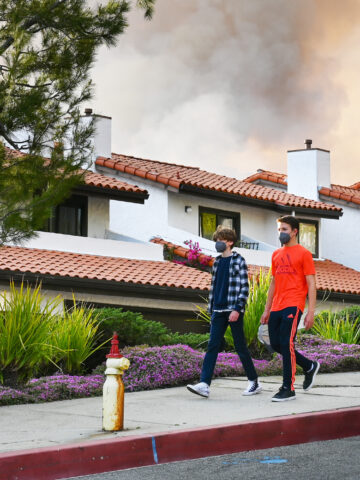 Two teens walk down the sidewalk with wildfire smoke in the background