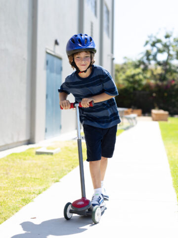 Child rides scooter on sidewalk while wearing a helmet