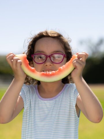 Girl with glasses holding watermelon rind to her face like a smile