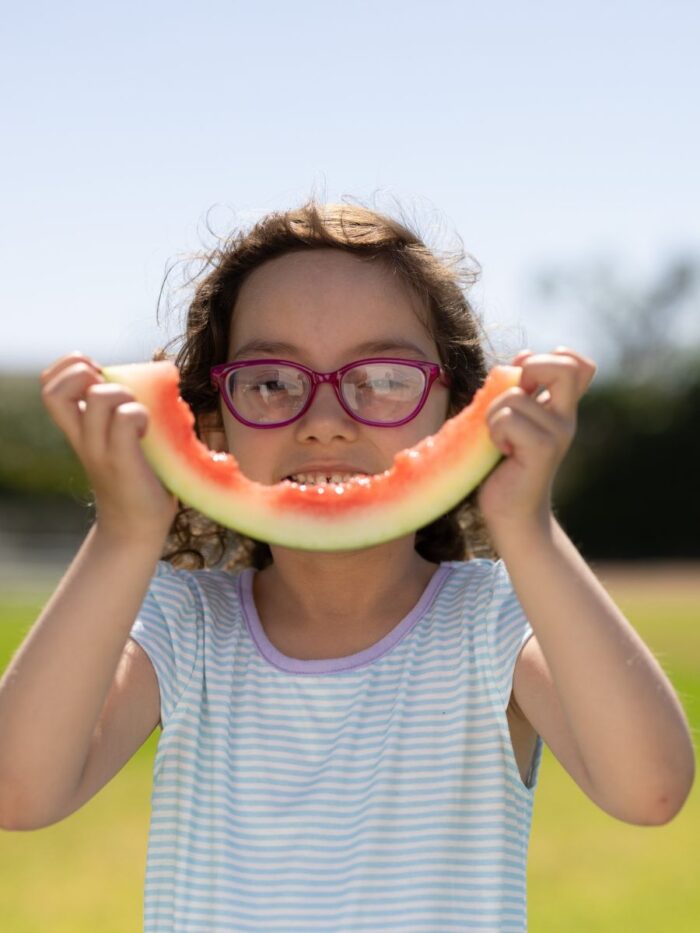 Girl with glasses holding watermelon rind to her face like a smile