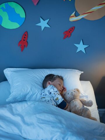 child sleeping in a bed with planets and stars decorating the walls