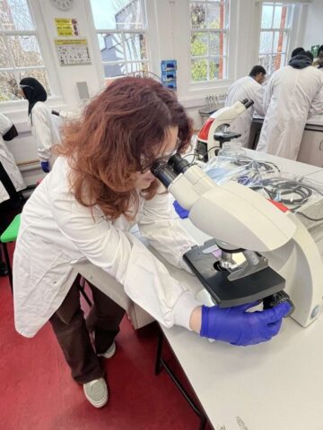 red headed woman wearing white lab coat looks at microscope