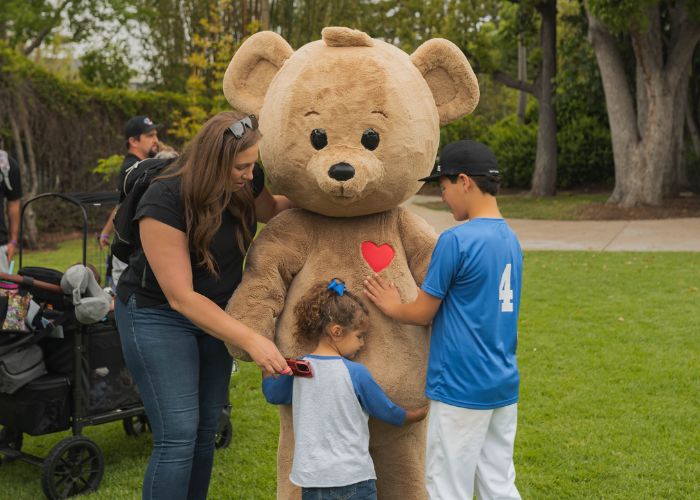 A mother and two children hug life-sized teddy bear
