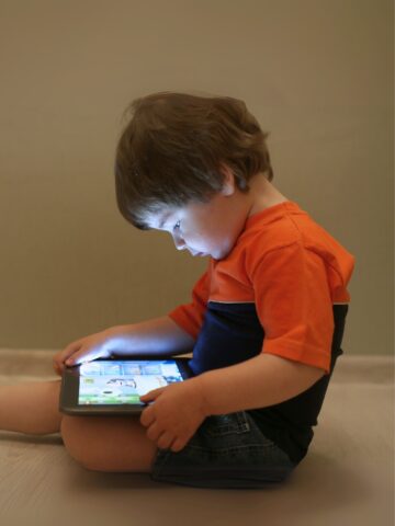 toddler with brown hair watches tablet in lap