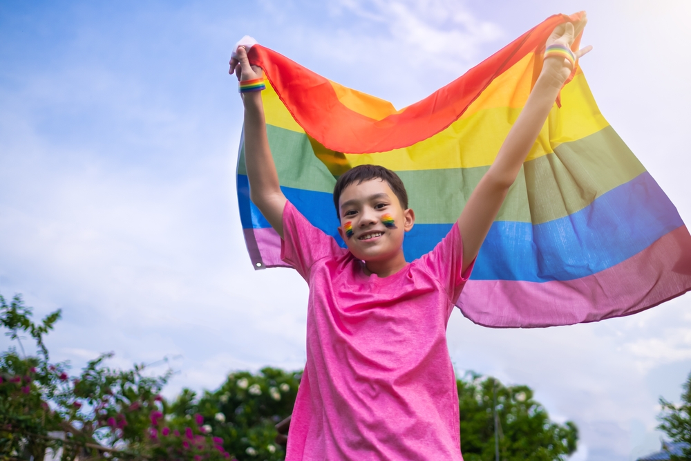 Youth holding rainbow flag with rainbow face paint