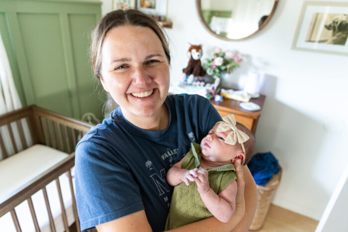 A smiling woman in a blue shirt holds her baby