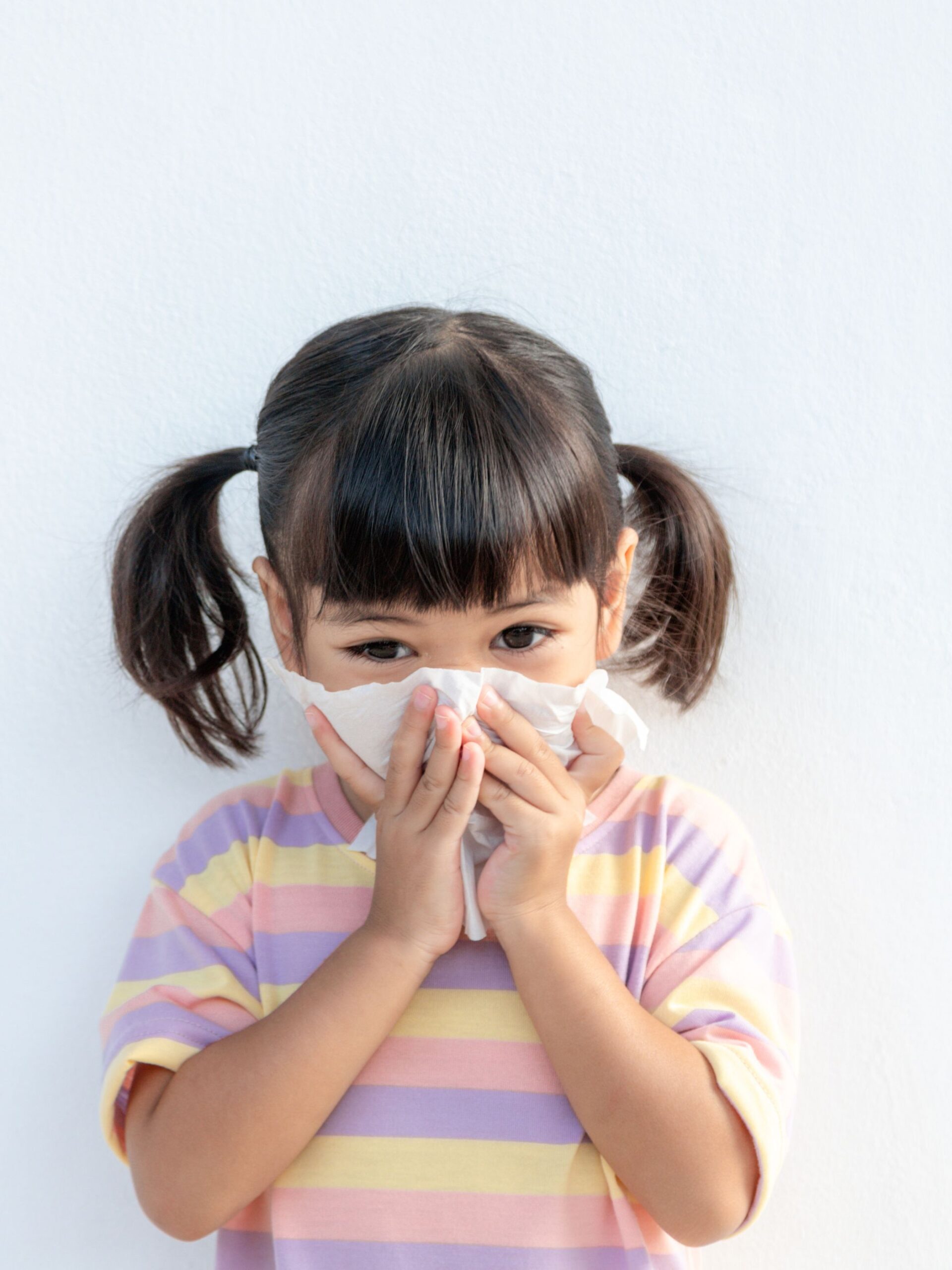 little girl with pigtails and pink shirt sneezes into tissue