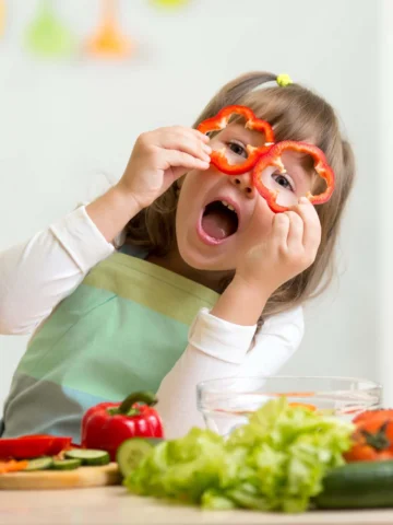 Child holding up bell peppers to eyes
