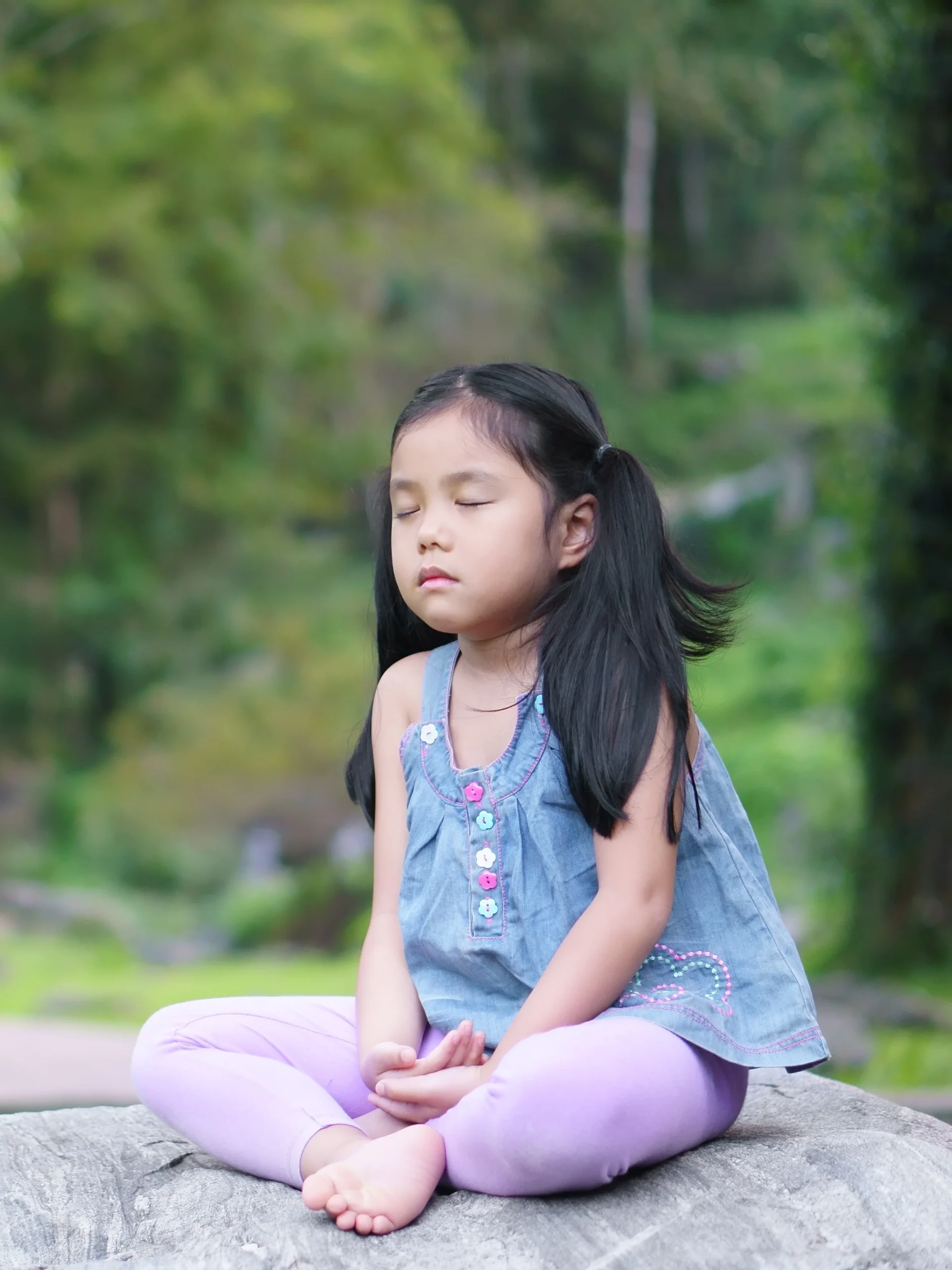 Child looks calm and peaceful while sitting on a rock - practicing mindfulness