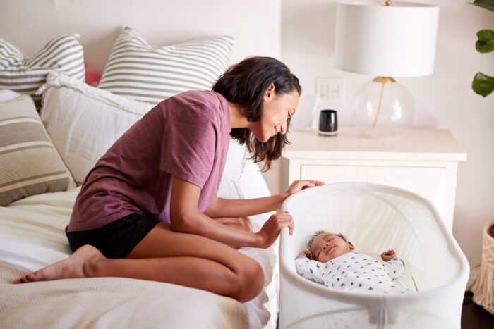 mom looking at sleeping newborn in bassinet