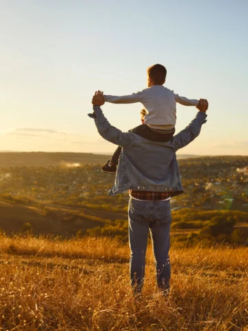 Child on parent's shoulders in nature 