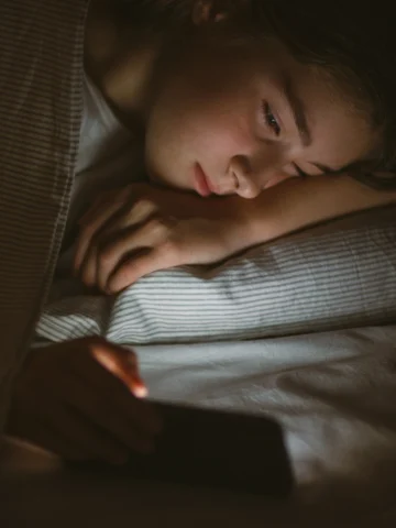 Teen looking a phone screen while in bed