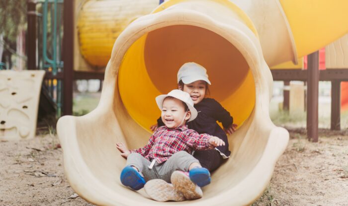 Two siblings having fun going down the slide together at the park.