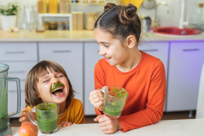 Happy Kids with glass cup of green smoothies in hands.