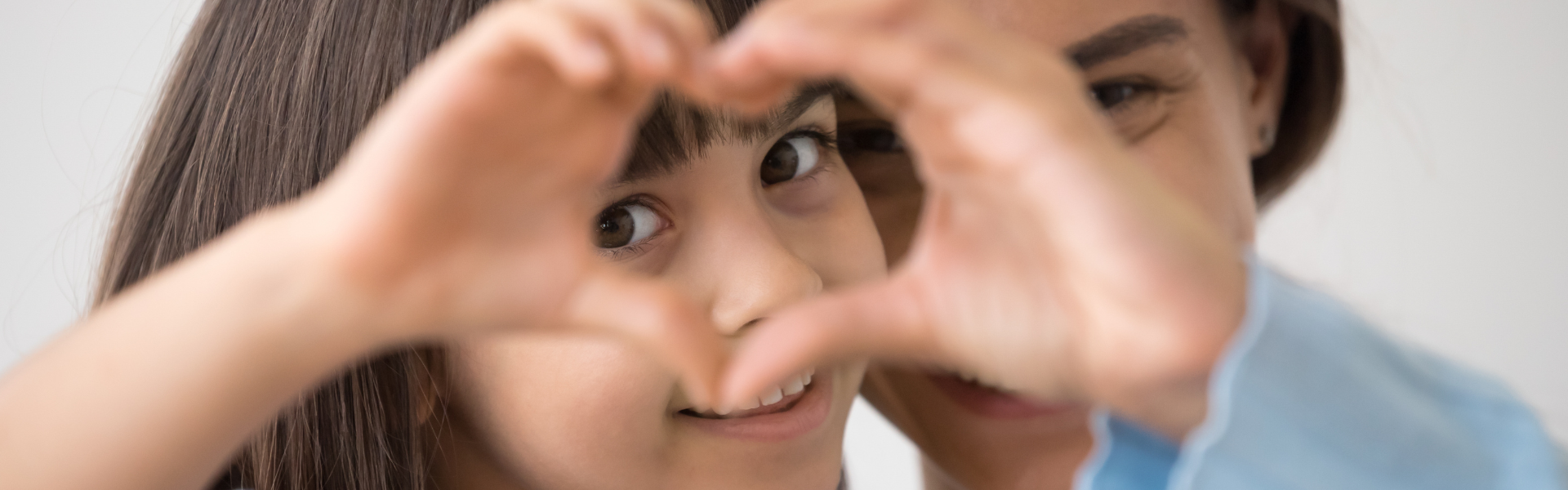 Girl with caretaker holding up a heart with her hands.