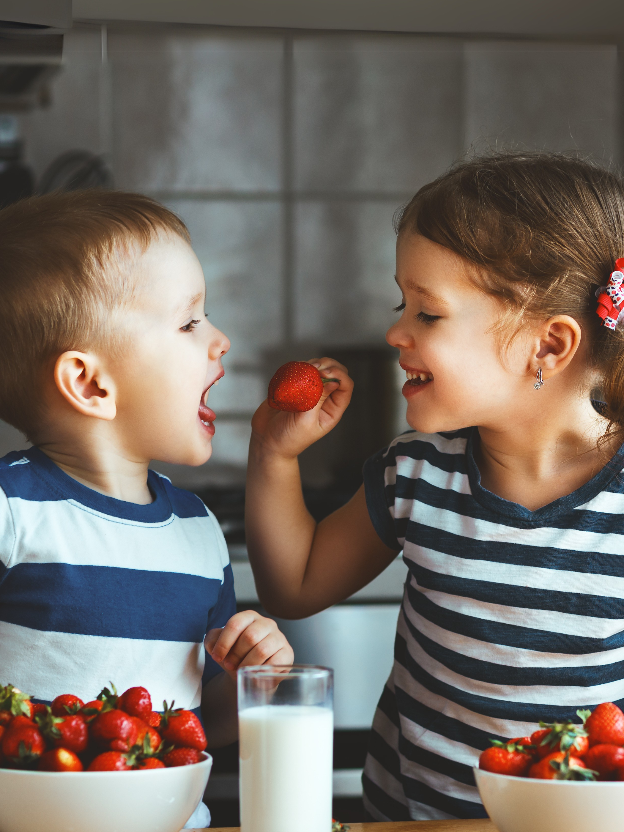 Happy children girl and boy brother and sister eating strawberries with milk