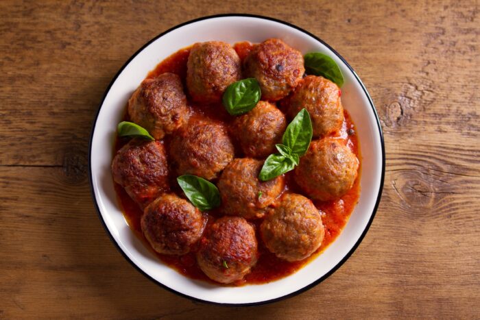 Meatballs in tomato sauce, garnished with basil in bowl on wooden table. 