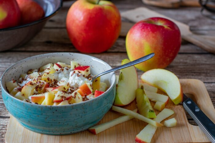 a Healthy breakfast bowl with cottage cheese and apples served with linseed on a wooden cutting board