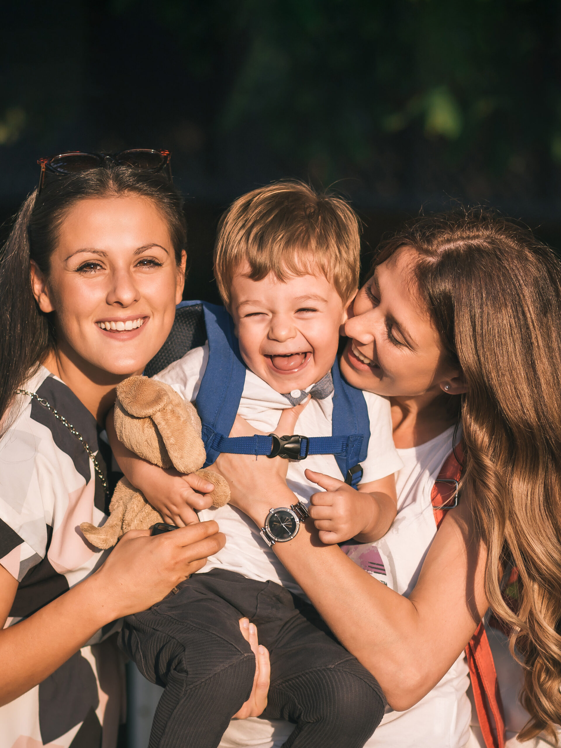 Boy laughs while two women hug him