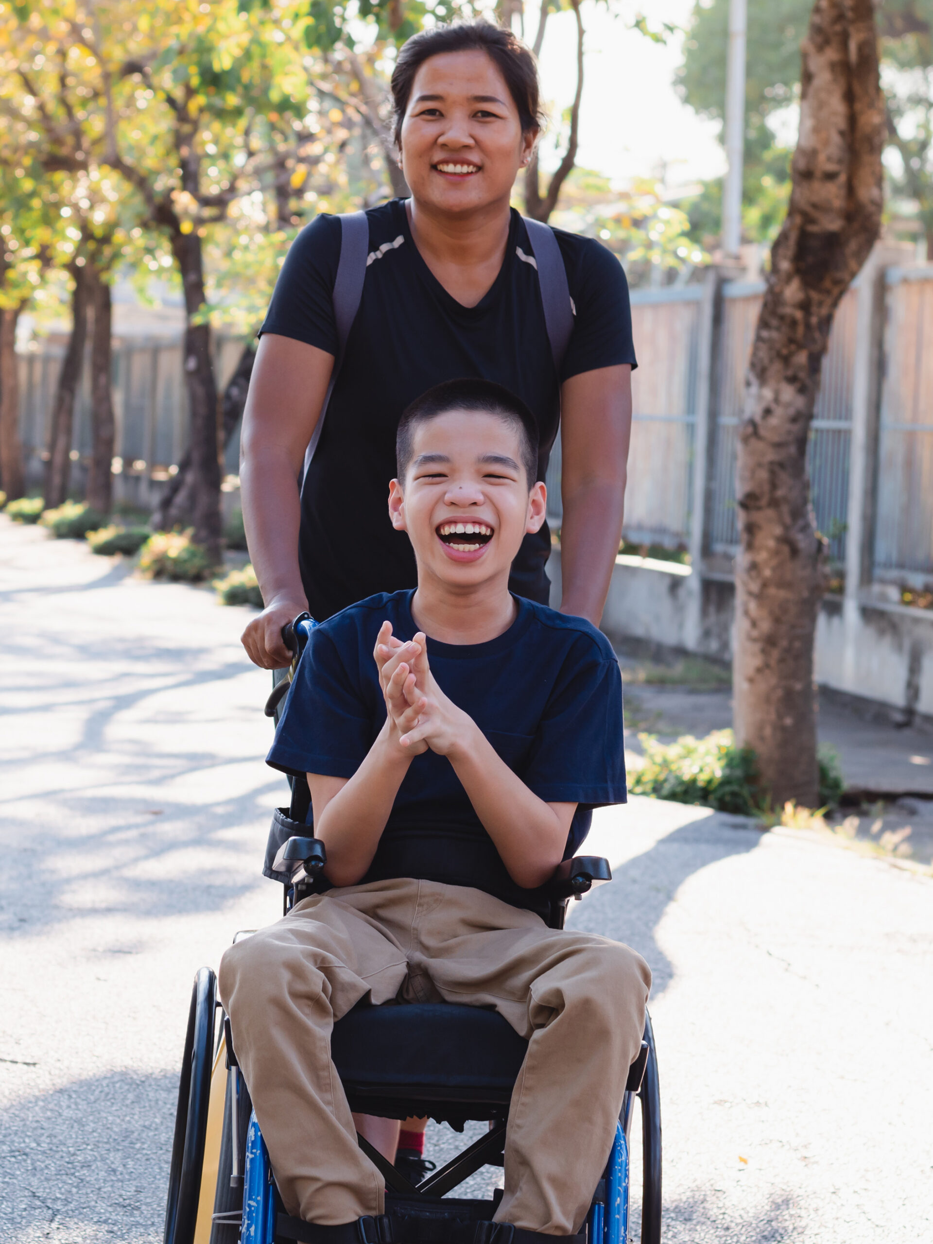 Child in wheelchair laughs and is pushed by smiling adult