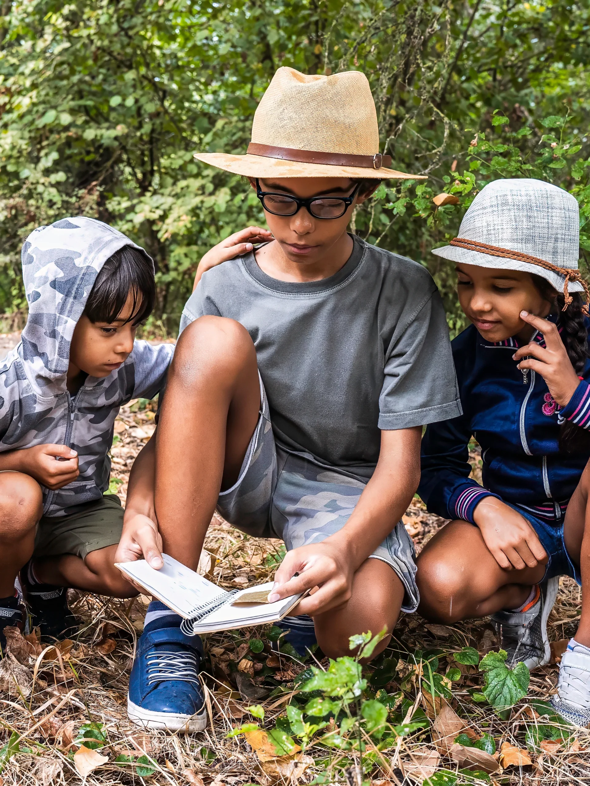 Group of three children in nature looking at notebook