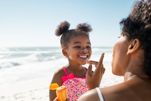 Young mother applying protective sunscreen on daughter nose at beach. prepare kids for summer travel