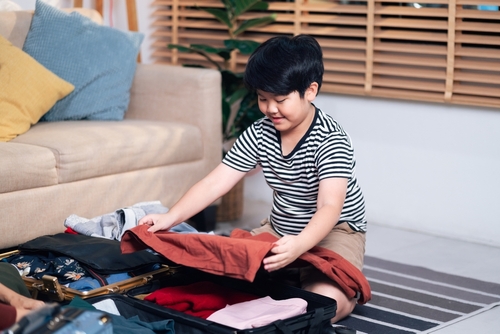Young Boy Organizing Clothes in a Suitcase for a Weekend Vacation, Capturing Moments of Family Travel Planning and Childhood Adventure