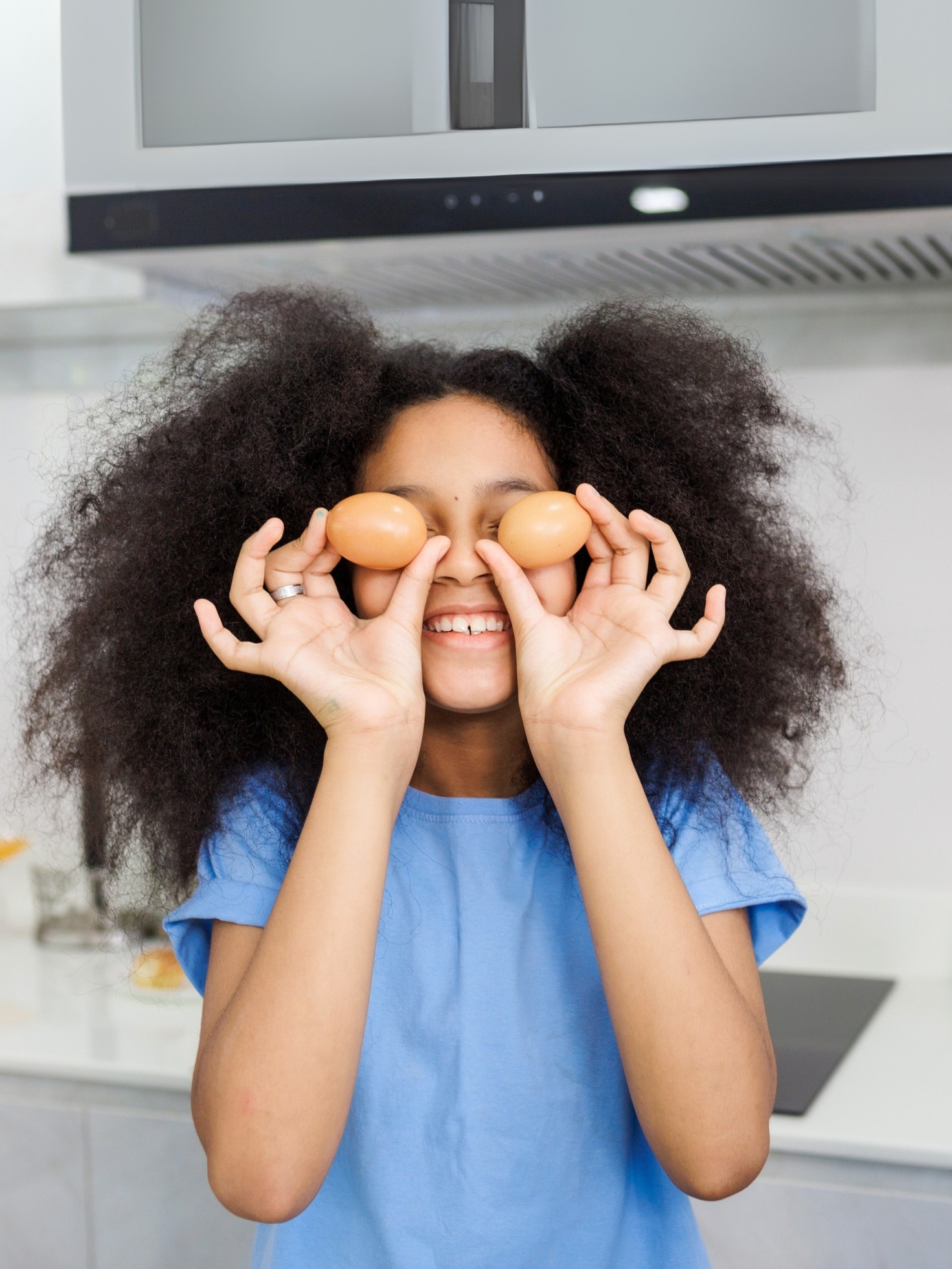 Child holds eggs near his eyes, cooking in kitchen. Kids entertainment. Healthy eating concept