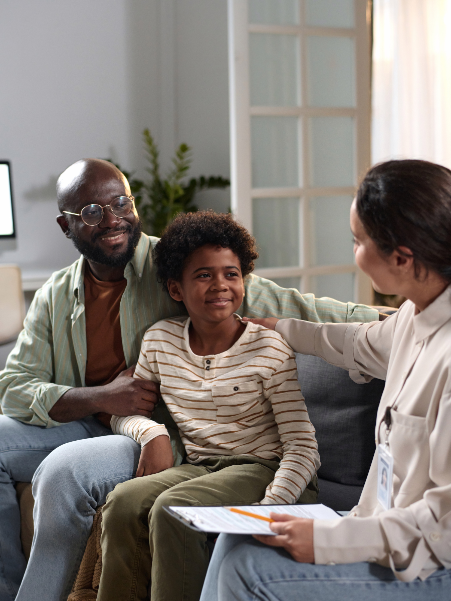 Vertical portrait of smiling young boy with father consulting with mental health specialist
