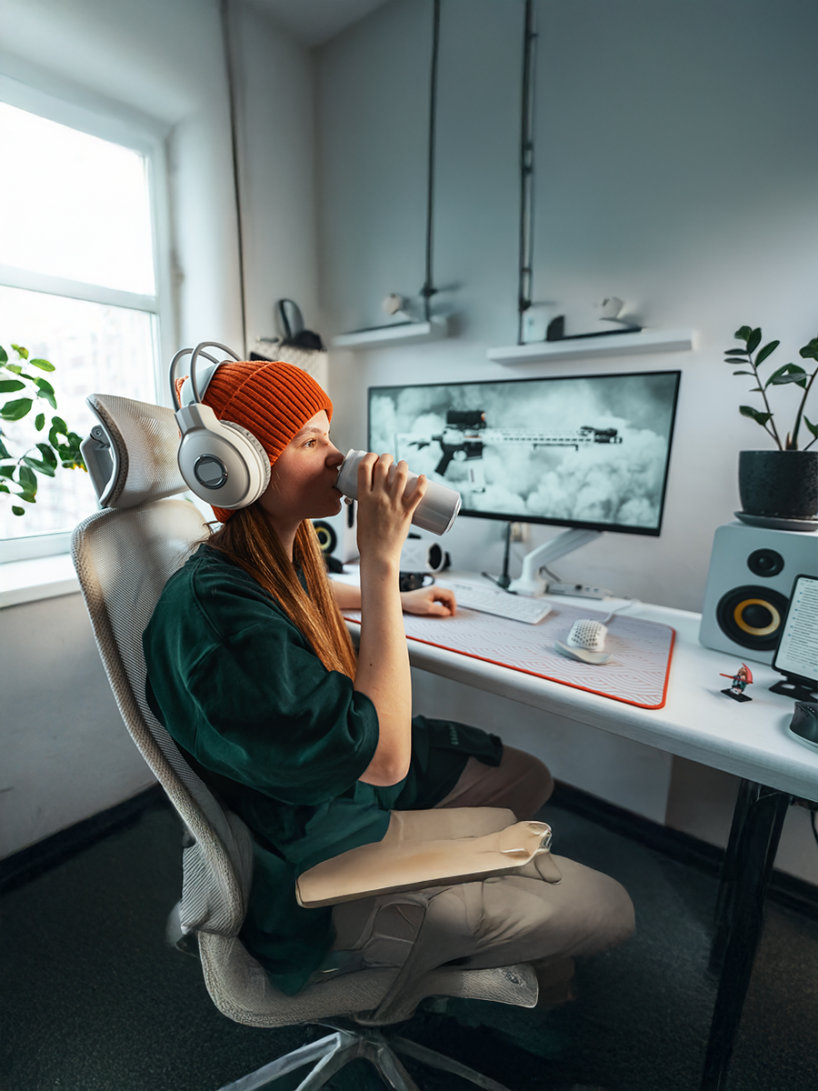 Gamer leans back in an adjustable chair while casually sipping an energy drink. Smart workstation setup supports both focused gameplay and relaxed moments between sessions.