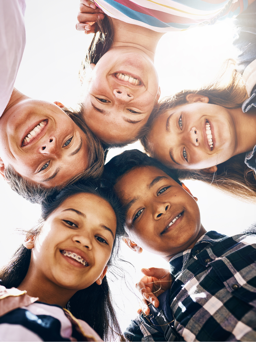 Group, portrait and happy children in school for education, support or development. Low angle, diversity and huddle of friends with smile in playground for solidarity, teamwork or playing together