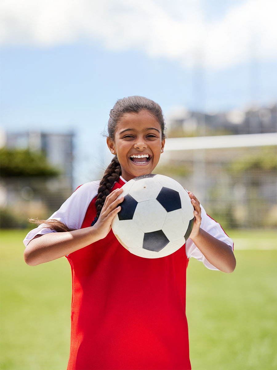 Soccer, sports and happy Indian girl athlete holding a sport ball on a school field. Portrait of fitness, football and exercise of a child smile excited about training, workout and game motivation