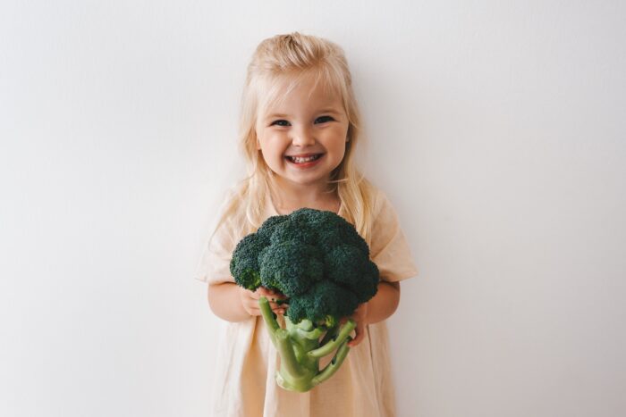 Child with broccoli healthy vegan food organic vegetables harvest plant based diet nutrition funny 3 years old girl happy smiling kid