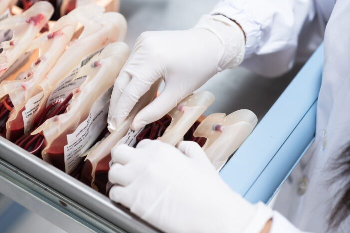 Close up scientist hand holding red blood bag in storage refrigerator at blood bank unit laboratory.Scientist selective and hand holding blood bag for save life patient.Medical treatment concept.