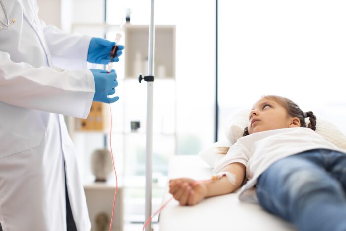 Young girl receiving blood transfusion in hospital setting, attended by doctor in medical uniform and gloves. Scene highlights medical care, health, and pediatric treatment.