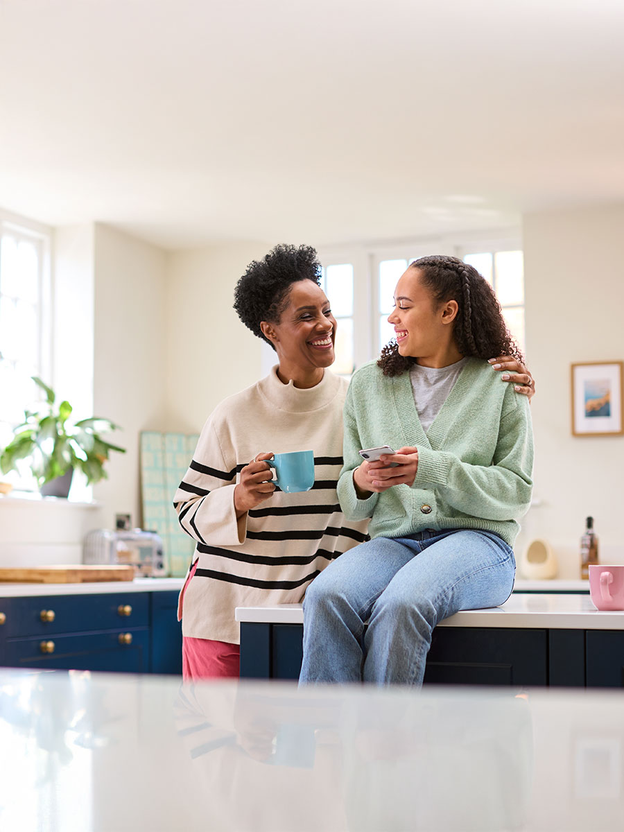 Mother Talking With Teenage Daughter At Home As She Checks Social Media On Mobile Phone
