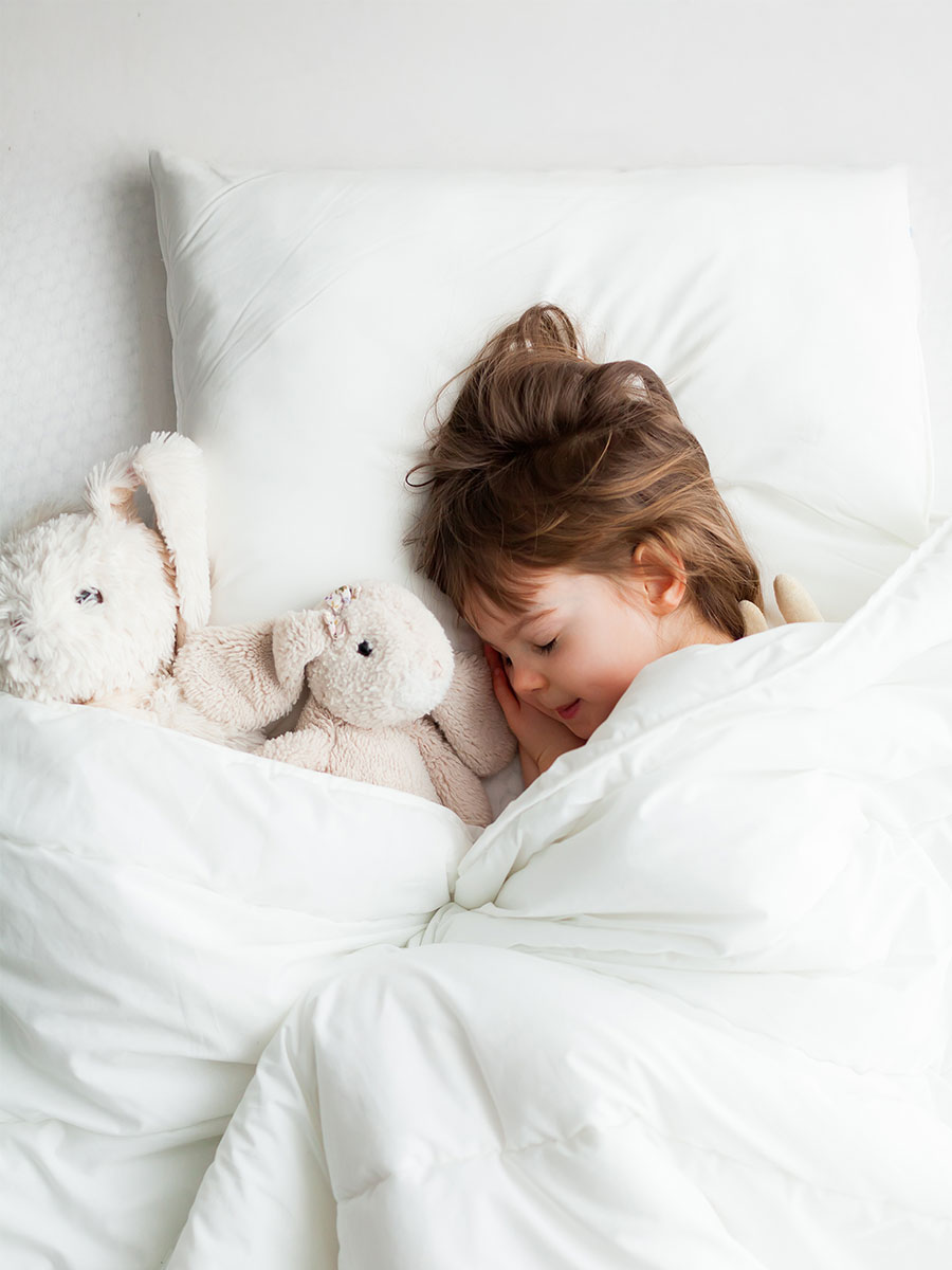 Sweet little girl sleeping in white bed with rabbit toys near her