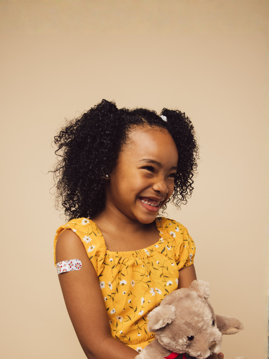Cute girl with bandage on arm after getting a vaccine smiling. Girl holding her teddy bear looking away and smiling after vaccination.