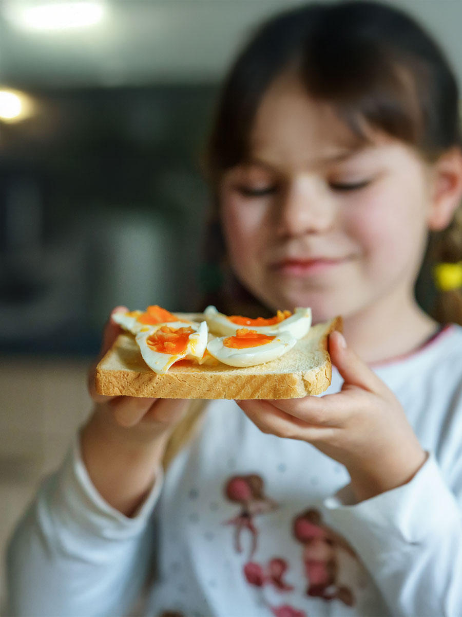 Little smiling girl have a breakfast at home. Preschool child eating sandwich with boiled eggs. Happy children, healthy food and meal.