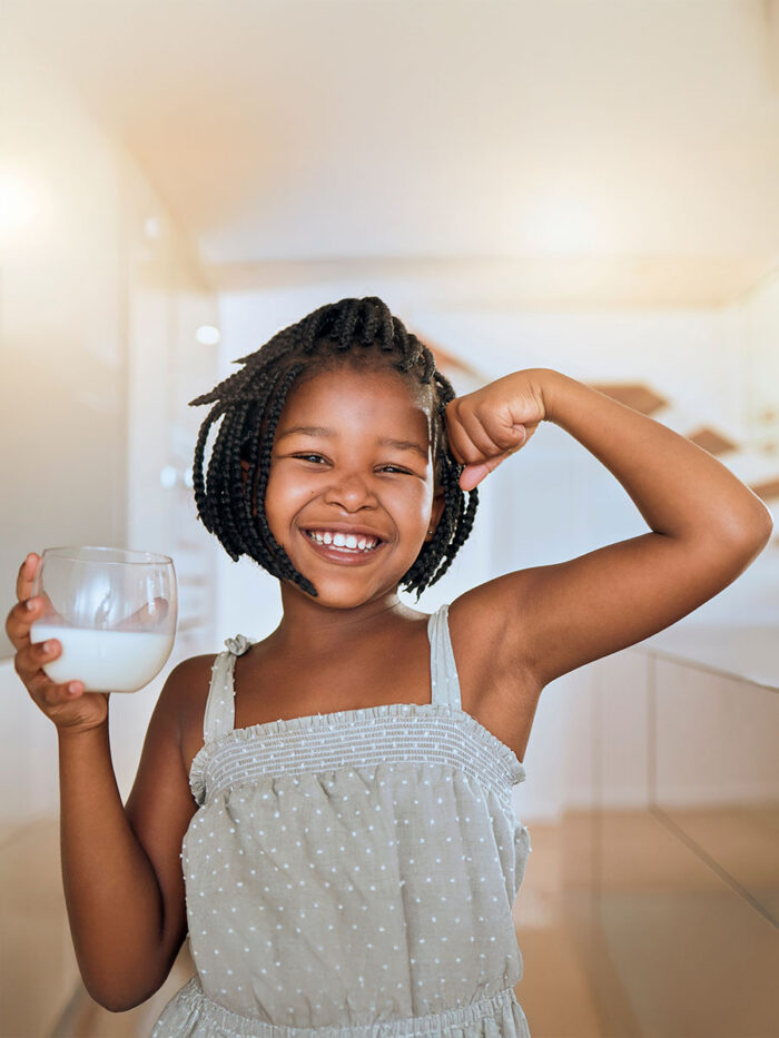 African girl with milk, picture and muscles from healthy drinks for energy, growth and nutrition in the kitchen. Happy, smile and flex baby's muscles with calcium in a glass and take care of health