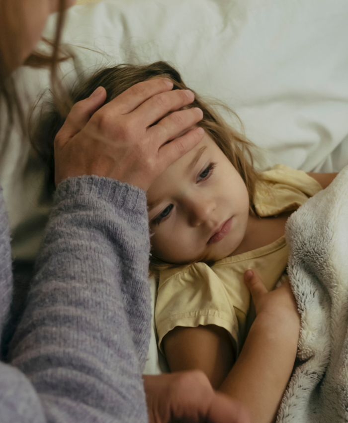 Sick child laying in bed with mother touching her forehead
