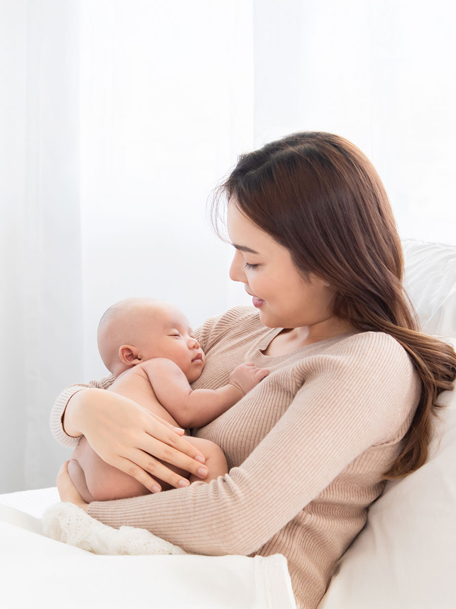 Mother holding newborn baby sleep on her lap, Young mom supports and tenderly cuddles adorable infant gently while infant sleeping on chest with safe and care.