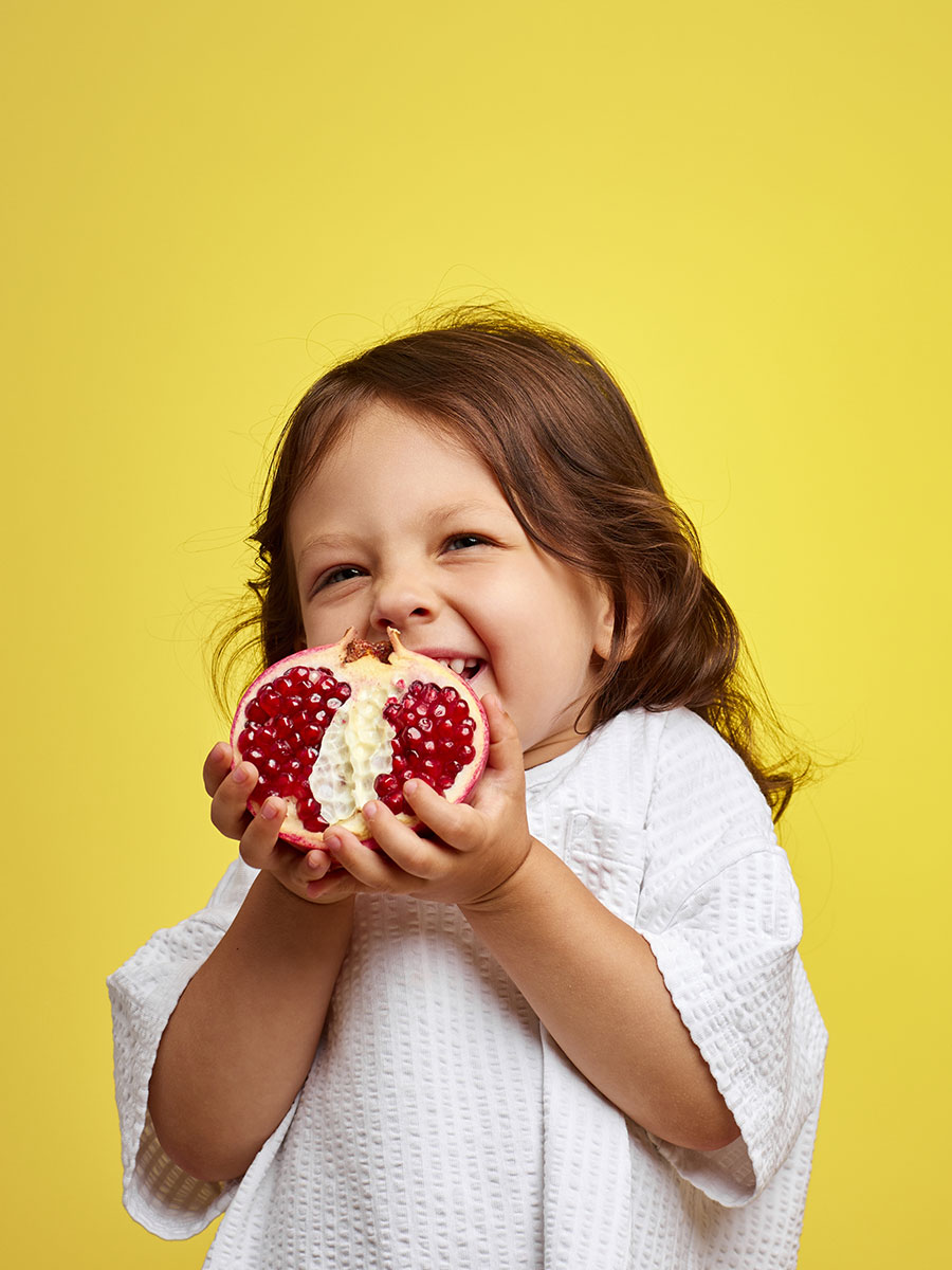 cute little child girl holding a pomegranate on yellow background.