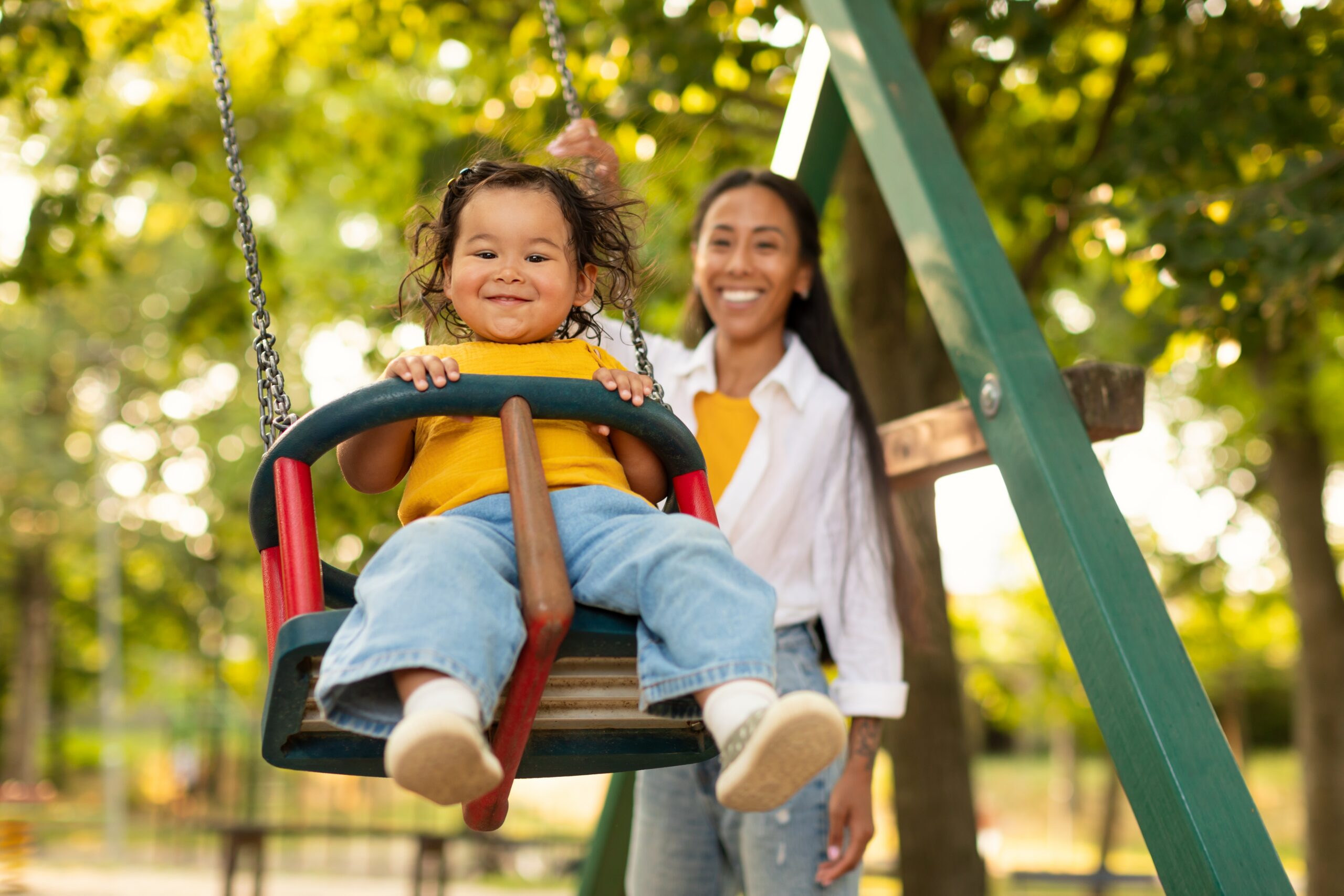 Smiling Korean Mother Swinging Baby Toddler Girl On The Swing, Riding Adorable Child Daughter And Having Fun On Outdoor Playground. Weekend With Mom, Activities For Mommy And Kid. Selective Focus