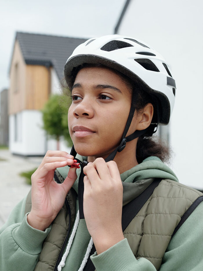 Serene African American postwoman fastening sports helmet while standing in front of camera in countryside and looking forwards